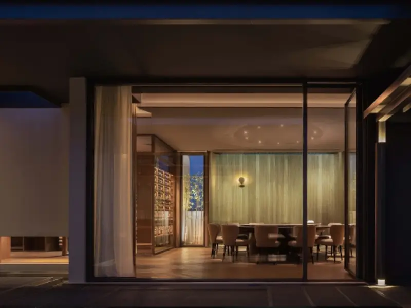 Side-hinged door open onto a dining area beside a lit pool at dusk