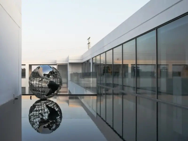 Glass curtain wall corridor beside a reflecting pool with a sculptural globe